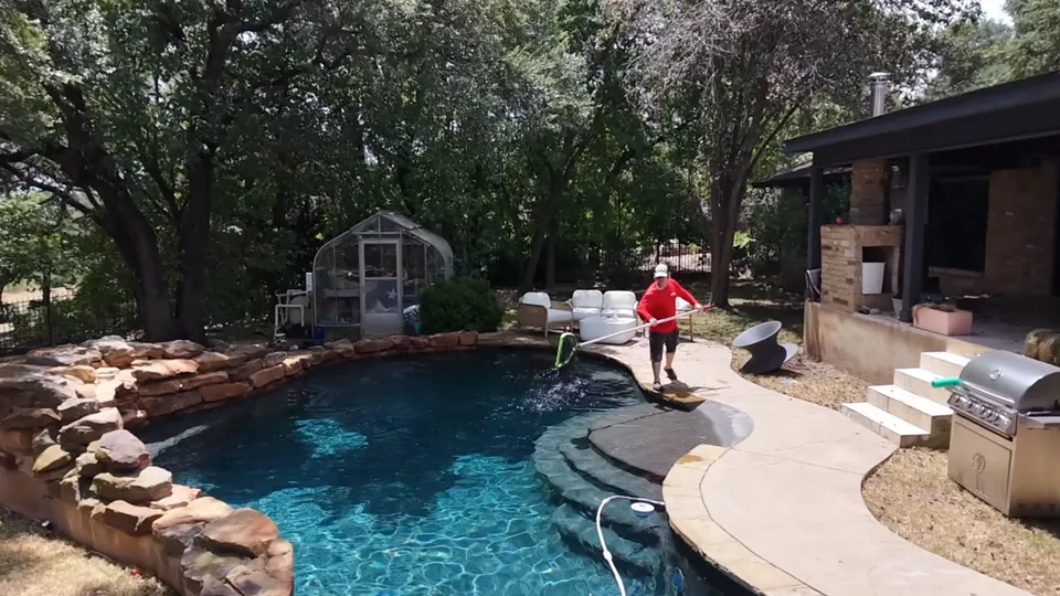 A Sullivan’s technician netting debris from a free-form pool with a stone edge, under oak trees