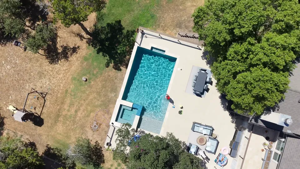 Aerial view of a rectangular backyard pool with an attached spa, surrounded by live oaks