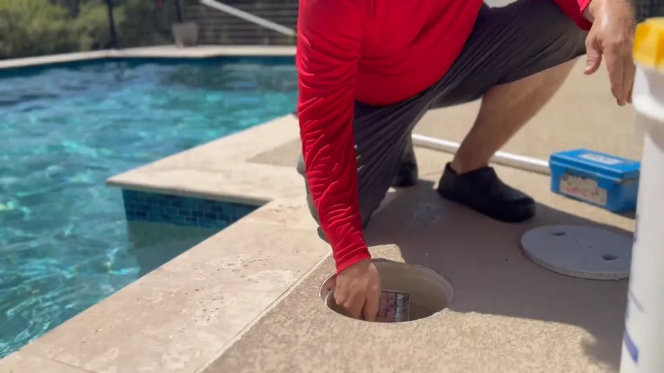 A Sullivan’s technician kneeling on the deck to empty a pool skimmer basket